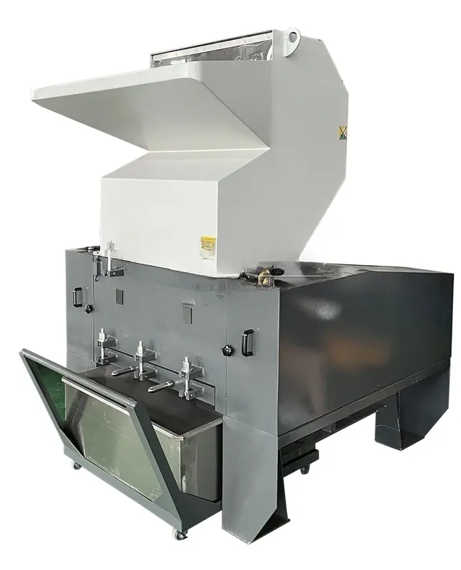 a Bottle Crusher Machine, specifically designed for reducing the volume of plastic bottles to facilitate more efficient recycling processes. The machine shown is robust, mainly in gray and features a large white hopper at the top where bottles are fed into the crusher. Below the hopper, the body houses the crushing mechanism, which compresses and crushes the bottles into smaller, manageable sizes. This type of machine is vital in waste management environments, particularly in places where the reduction of plastic waste volume is critical, such as in recycling centers, manufacturing facilities, and even large commercial establishments.