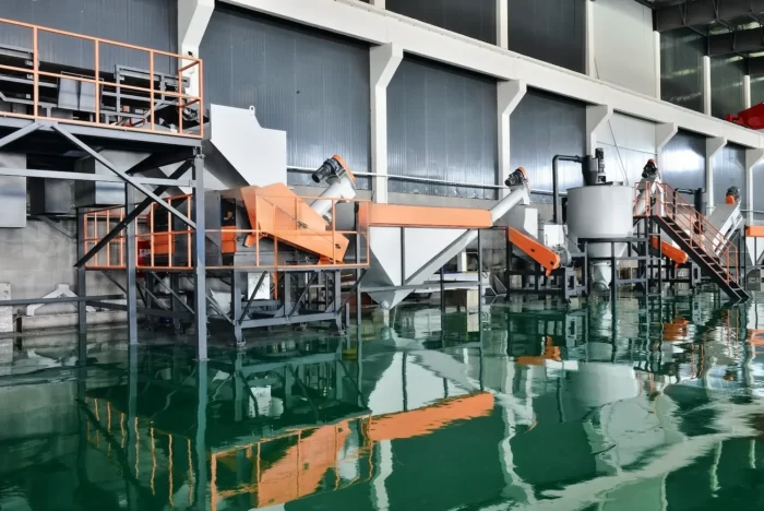 depicts a sophisticated plastic recycling facility equipped with LDPE (Low-Density Polyethylene) recycling equipment. The setup features various machines including conveyors, crushers, and wash stations that are strategically placed over a large water tank for the separation and washing of recycled materials. The system's framework is painted in a mix of gray and orange, providing a stark contrast to the industrial background. This type of facility is typically used for the recycling of soft plastics, such as plastic bags and films, which undergo processes including shredding, washing, and drying to prepare them for reintegration into the production cycle. The presence of the water tank is indicative of the washing process, where plastics are cleansed of impurities such as soil, labels, and adhesives. Facilities like this play a crucial role in minimizing waste and promoting sustainable practices within the plastics industry.
